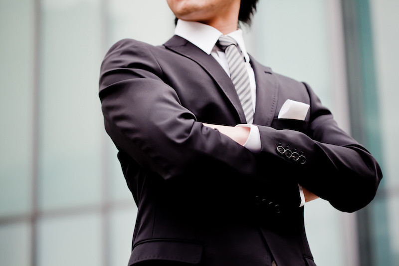 腕を組んでいるスーツ姿の男性